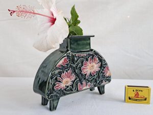 Dark green ceramic vase with glossy finish, featuring embossed pink and light red floral patterns and green leaves, holding a white hibiscus with a pink center, in a vintage artisanal style. Handmade by Jo Ceramics
